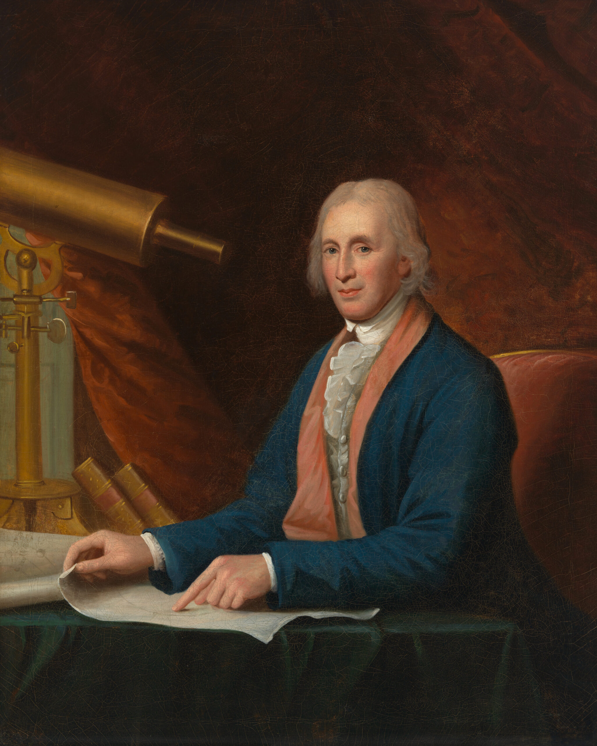 David Rittenhouse seated beside a large telescope with astronomical charts spread across a table.