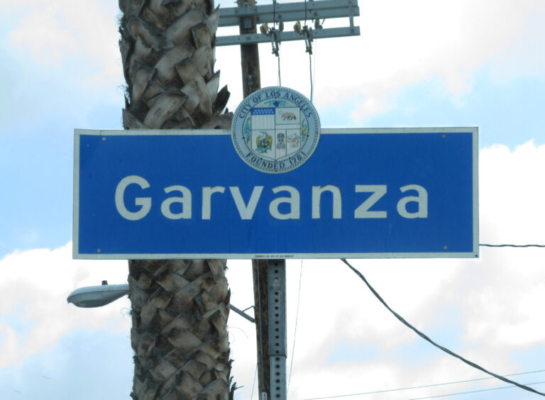 Blue Garvanza neighborhood sign on York Boulevard at Figueroa Street in Los Angeles, with a palm tree behind it.