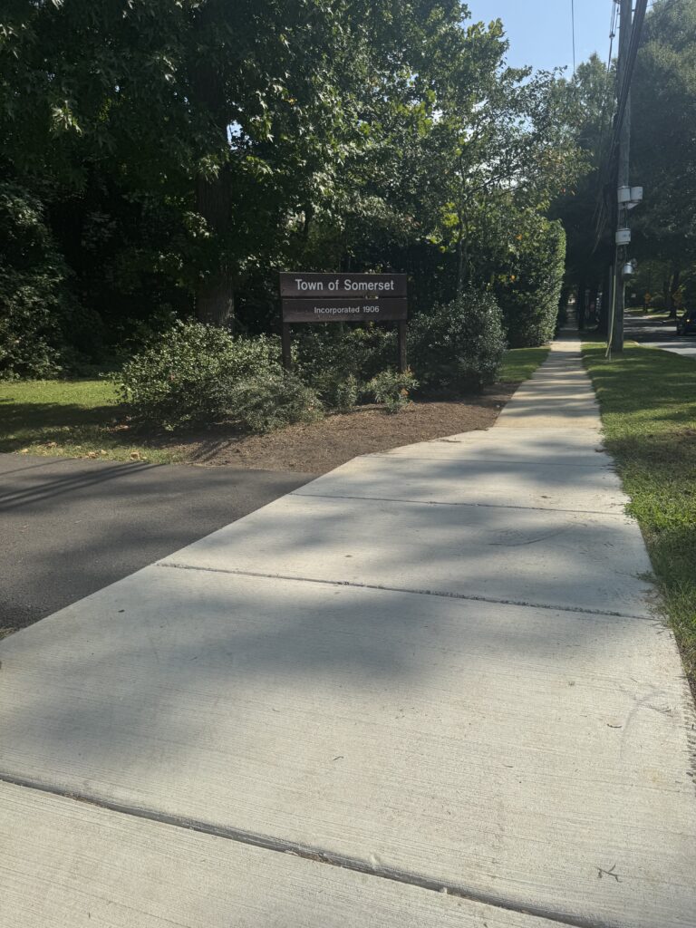 Sidewalk entering the Town of Somerset beside a town boundary sign and wooded parkland.