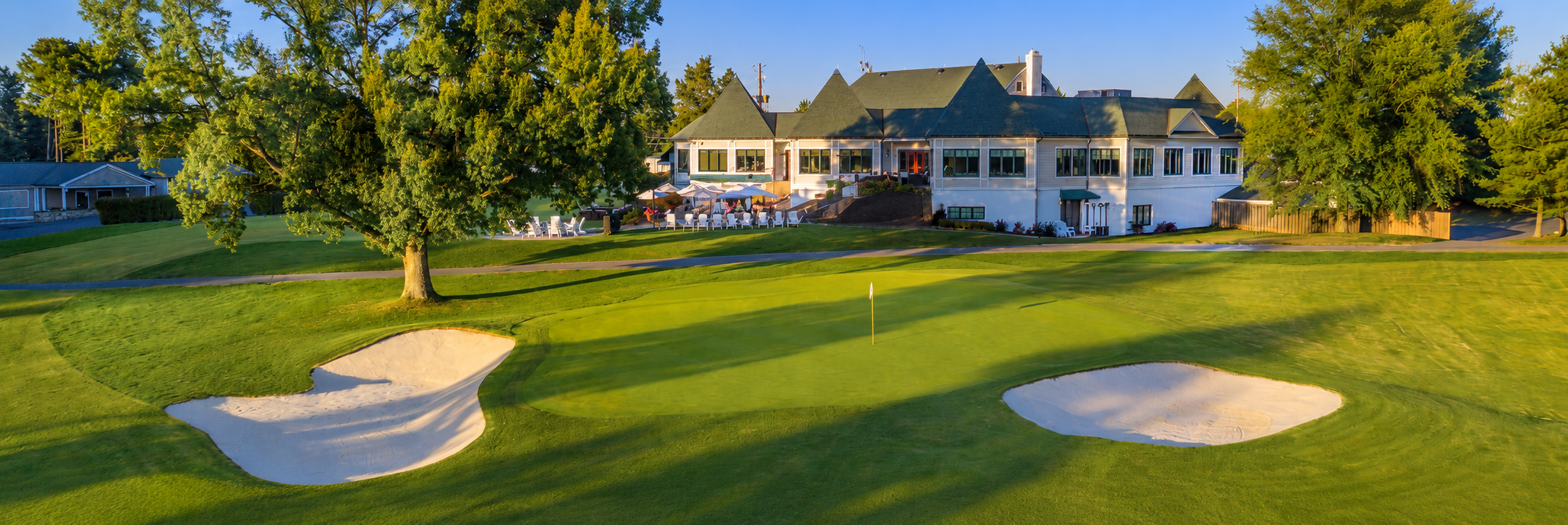 The 18th green at Argyle Country Club, flanked by two bunkers with a large oak tree to the left and the clubhouse behind.